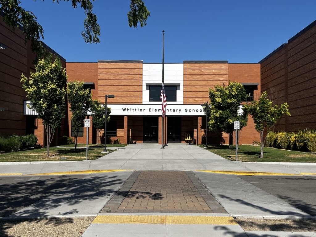 The front of Whittier Elementary School in Boise Idaho with trees and a flag pole in the foreground
