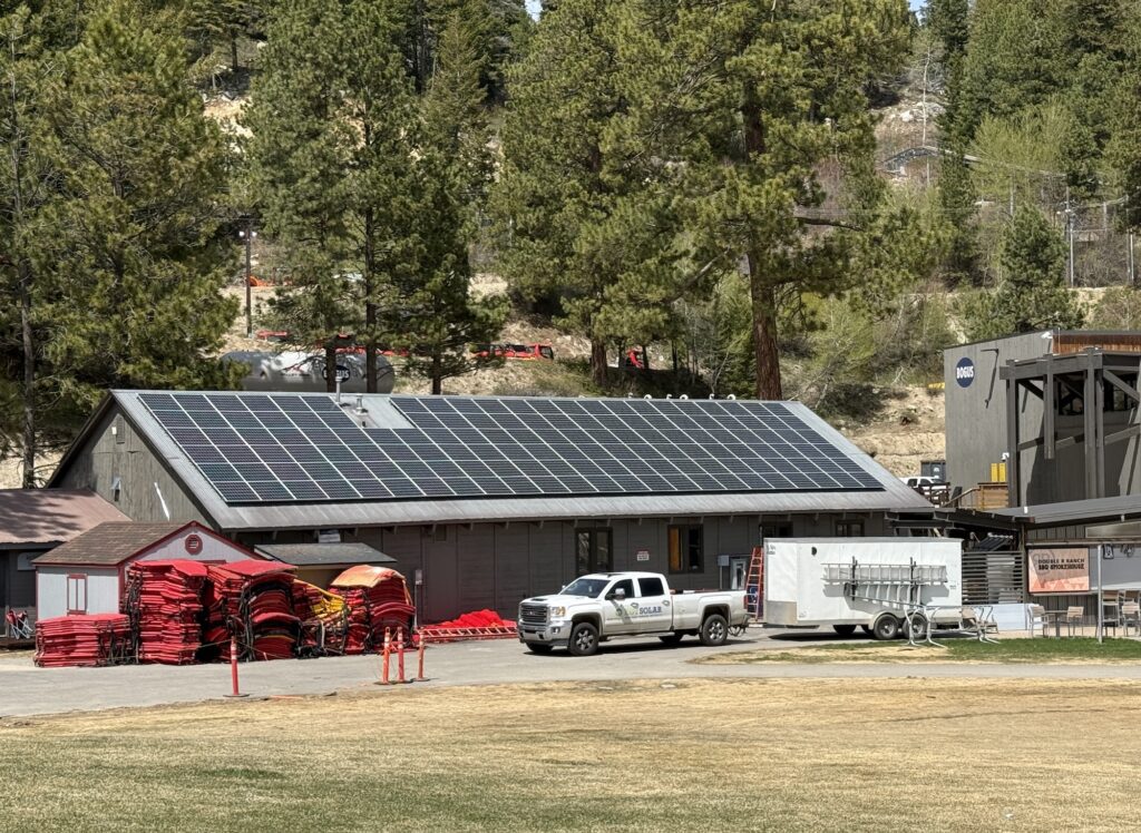 Solar panels on the roof of Bogus Basin's rental shop, with a truck and trailer out front that have EGT Solar logo on them, and pine trees behind the building